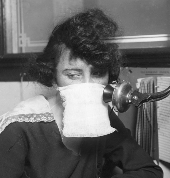 Black and white photo of a white female telephone operator wearing a mask.