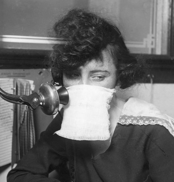 Black and white photo of a white female telephone operator wearing a mask.